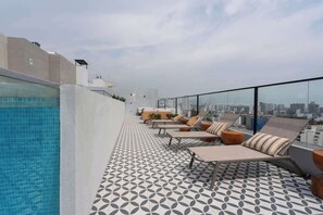Un área de piscina en la azotea con sillones reclinables y suelo estampado.