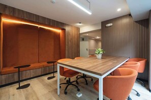 Una sala de conferencias moderna con una mesa de madera, sillas naranjas, un banco y una planta en maceta.