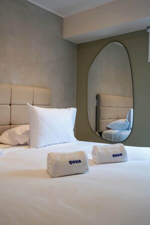 Habitación de hotel con cama, almohadas, un espejo redondo y una toalla con la marca 'geko'.