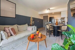 A modern living room with a sofa, a round coffee table with candles, and a dining area with chairs and a table.