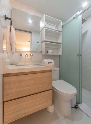 Ein modernes Badezimmer mit weißem Waschbecken, Spiegel und Toilette, Holzschränken und einer Glasdusche.