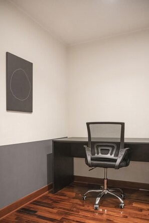 Ein Büro im Eckbereich mit einem schwarzen Mesh-Stuhl, einem dunklen Schreibtisch und einem gerahmten Bild an der Wand.