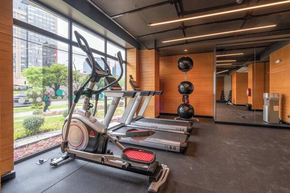 Une salle de sport équipée de tapis de course, d’un vélo elliptique et d’un vélo d’appartement, avec de grandes fenêtres et une vue sur l’extérieur.
