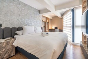 Une chambre d’hôtel moderne dotée d’un grand lit, d’une table de chevet en bois, d’un téléviseur intégré et d’un mur au motif de pierres.