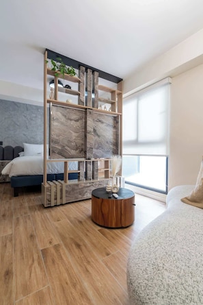 Un dormitorio moderno con cama, una mesa redonda de madera, un biombo decorativo y un ventanal grande.
