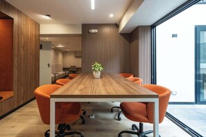 Un salón de conferencias con una mesa de madera, sillas anaranjadas, una planta en maceta y un amplio ventanal.