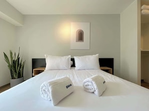 A hotel room with a neatly made bed, a potted plant, and a framed picture on the wall.