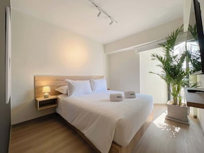 A modern hotel room with a large bed, bedside tables, a lamp, a potted plant, and a TV.