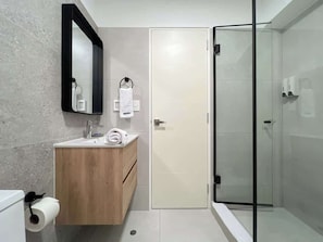 A modern bathroom with a wooden vanity, a glass shower enclosure, and a white door.
