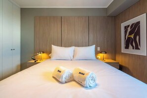 A hotel room with a bed, two bedside lamps, a wooden headboard, and a framed artwork on the wall.
