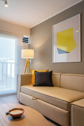 A modern living room with a sofa, a floor lamp, a wall art piece, and a view through a large window. - Geko| Sleek 1BR w/Balcony near Spots in Miraflores (Lima)