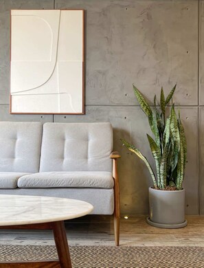 Una sala de estar moderna con un sofá, una mesa de centro, una planta en maceta y un cuadro abstracto grande en la pared.
