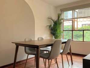 Un comedor con una mesa y sillas, una planta en maceta y una ventana que ofrece vistas al verdor.