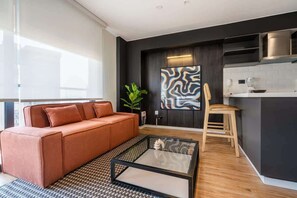 A modern living room with a sofa, a coffee table, and a kitchen area with a countertop and cabinets.