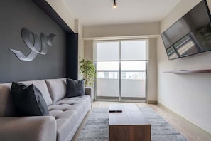 A modern living room with a sofa, a coffee table, a TV, and a large window.