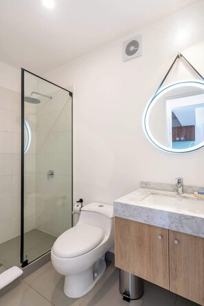 A modern bathroom with a glass-enclosed shower, a toilet, and a vanity with a marble countertop. - Geko | Modern 1BR in San Isidro Central Area (San Isidro)