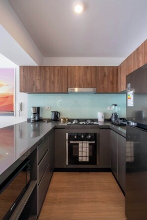 A modern kitchen with wooden cabinets, a stainless steel range, a built-in oven, and a refrigerator. - Geko | Modern 1BR in San Isidro Central Area (San Isidro)