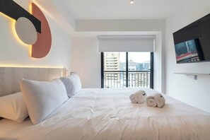 A modern hotel room with a large bed, a TV mounted on the wall, and a view of the city through the window. - Geko | Modern 1BR in San Isidro Central Area (San Isidro)