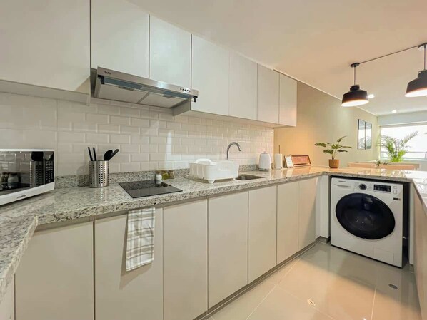 A modern kitchen with a built-in microwave, a sink, a stove, and a washing machine.