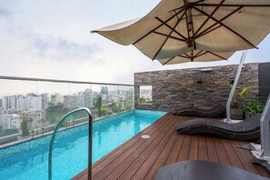 Ein Pool auf dem Dach mit einer Holzterrasse, Liegestühlen und einer Steinmauer.