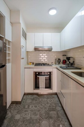 Una cocina compacta con gabinetes blancos, estufa a gas, horno y salpicadero de azulejos.