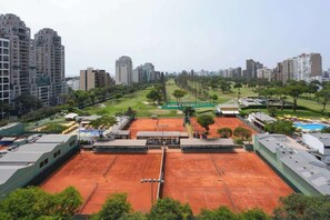 Un court de tennis entouré d’immeubles de grande hauteur, d’un espace vert et d’une piscine.