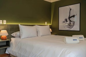 Habitación de hotel con cama, dos lámparas de noche, una obra de arte enmarco y dos toallas con el nombre de la marca.