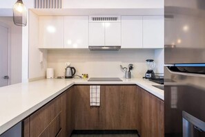 Eine moderne Küche mit weißen Schränken, einer Edelstahl-Dunstabzugshaube, einer Kaffeemaschine, einem Mixer und einem Wasserkocher.
