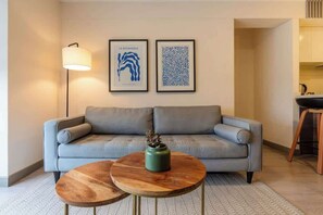 Ein Wohnzimmer mit einer Couch, zwei Holznachttischen, einer Stehlampe und zwei gerahmten Kunstwerken an der Wand.