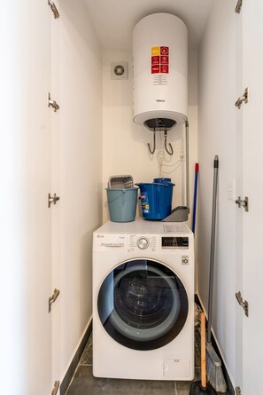 Ein kleiner Hauswirtschaftsraum mit einer Frontlader-Waschmaschine, einer Wandheizung und einem blauen Eimer.