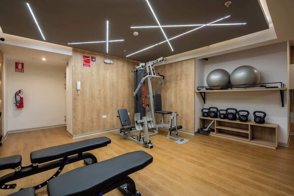 Une salle de sport équipée de machines d’exercice, de bancs et de kettlebells.