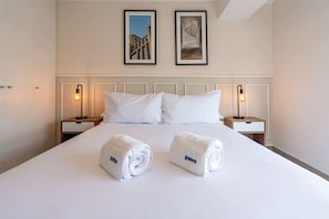Ein Hotelzimmer mit einem großen Bett, zwei Kissen, zwei Nachttischen mit Lampen und zwei zusammengerollten Handtüchern auf dem Bett.