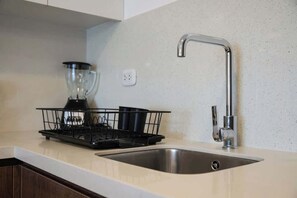Eine Küche mit einer Edelstahl-Spüle, einem schwarzen Geschirrgestell und einem Mixer auf der Arbeitsplatte.