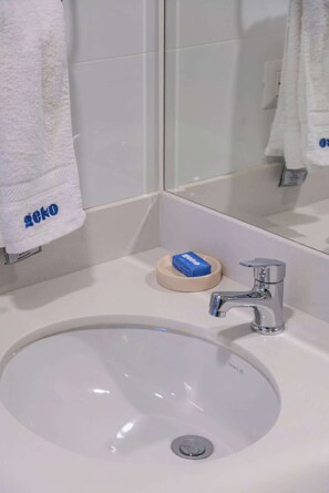Ein Badezimmer mit weißem Waschbecken, einem Spiegel und einem Handtuchhalter.