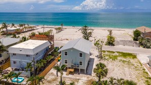 A beachfront property with a large house, a pool, and a sandy beach.