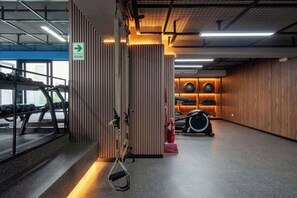 Ein Fitnessraum mit Trainingsgeräten, einem Feuerlöscher und einem Schild, das den Ausgang weist.