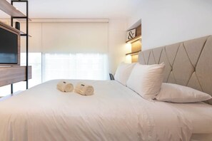 Una habitación de hotel con cama, almohadas, televisor y estante en la pared.