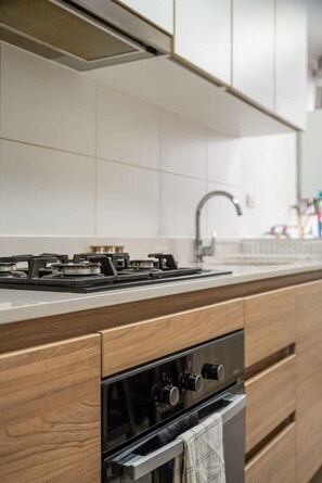 A kitchen with a gas stove, oven, and wooden cabinetry. - Geko | Central 2BR Flat in Barranco w/Balcony (Lima)