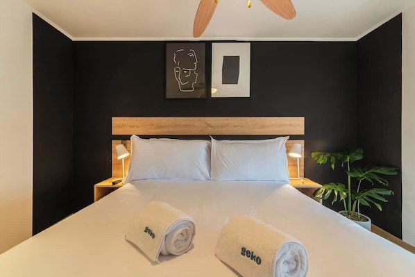 A hotel room with a large bed, two bedside lamps, a ceiling fan, a potted plant, and artwork on the wall. - Geko | Central 2BR Flat in Barranco w/Balcony (Lima)