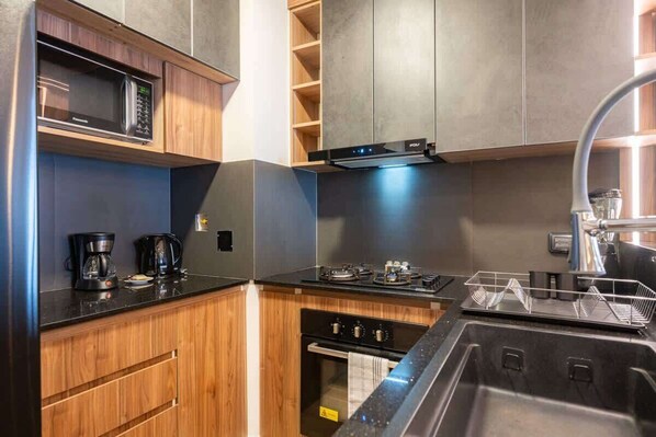 Une cuisine compacte dotée d’appareils électroménagers intégrés, de meubles en bois et d’un évier en acier inoxydable.