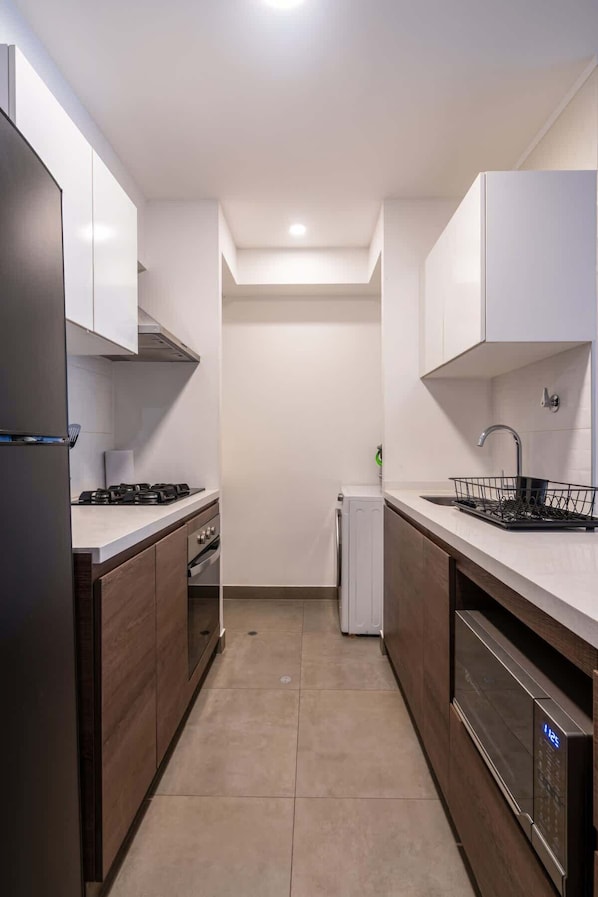 Una cocina moderna con armarios blancos, estufa integrada, lavavajillas y un refrigerador pequeño.