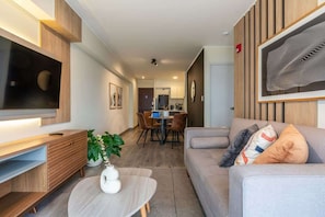 Una sala moderna con un televisor de pantalla plana, un sofá, una mesa de centro y un comedor con sillas y una mesa.