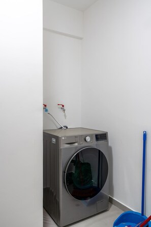 A compact, modern laundry room with a front-loading washing machine, a blue mop, and a red and blue water faucet.