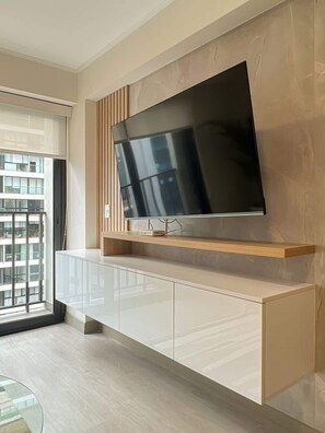 A modern living room with a large flat-screen TV mounted on a wooden shelf above a white cabinet.