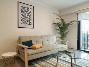 A living room with a sofa, a round table, a potted plant, and a framed artwork on the wall. - Geko | Elegant 1BR w/ Pool near San Isidro (San Isidro)