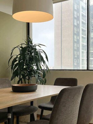 Un comedor con una mesa, sillas, una planta en maceta y un ventanal con vistas a edificios.