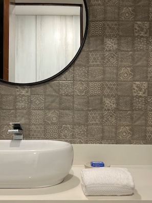 Un baño con un espejo redondo, un lavamanos blanco, baldosas con diseño y una toalla sobre la encimera.