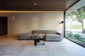 Ein modernes Interieur mit einer Eckcouch, einem kleinen Tisch und einem großen Fenster mit Blick auf Grünflächen.