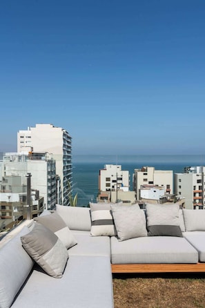 Ein moderner Außenbereich zum Sitzen mit Blick auf das Meer und die Stadtlandschaft.