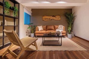 Un salon moderne avec un canapé en cuir, un fauteuil en osier, une table basse et une bibliothèque agrémentée de plantes.